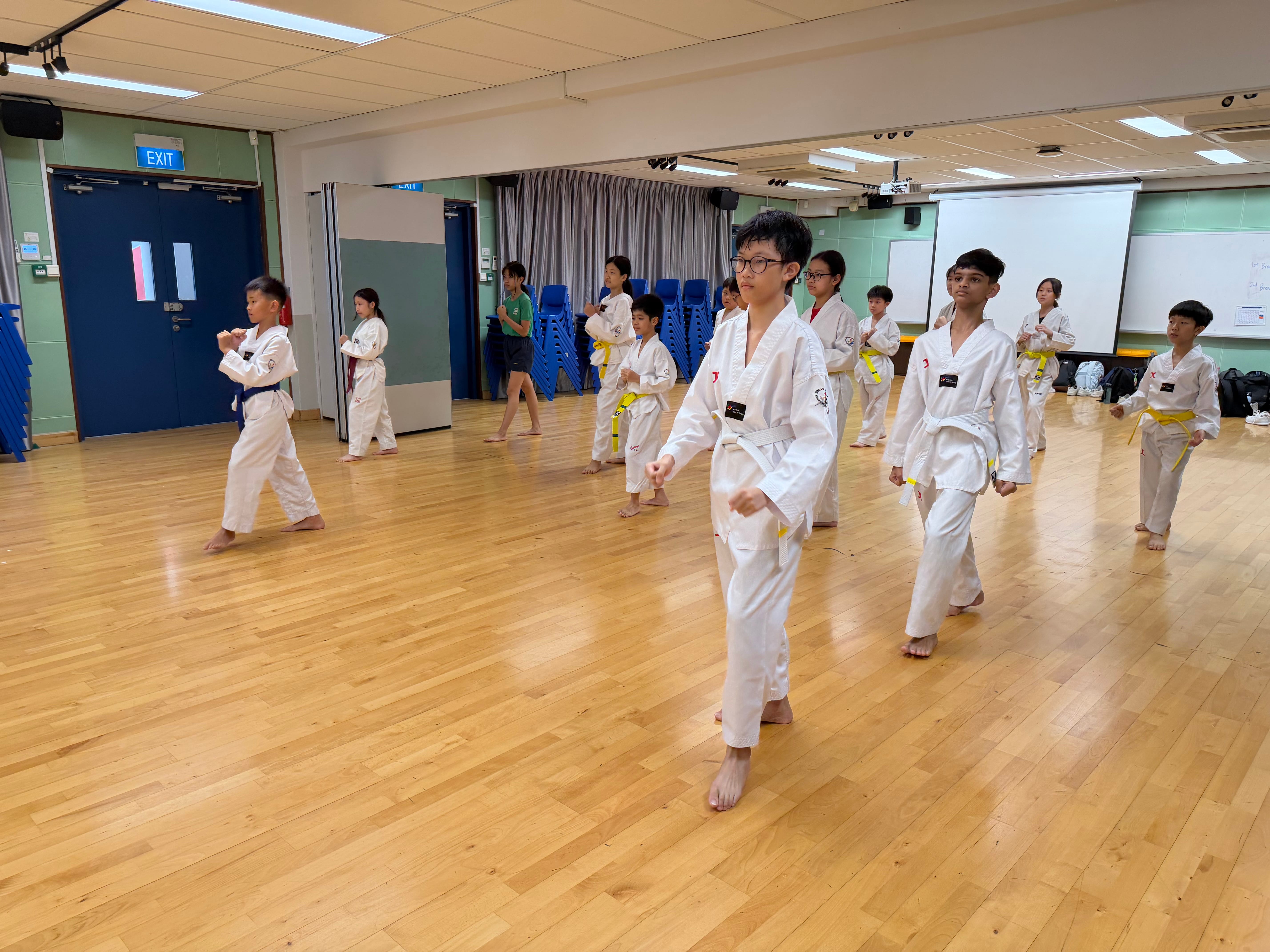 Students in their dobok practising taekwondo moves in an airconditioned room.